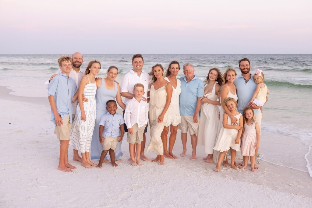 A multi-family photograph of 16 people taken on 30a as they wear an assortement of pastel blues, khaki and cream colors.