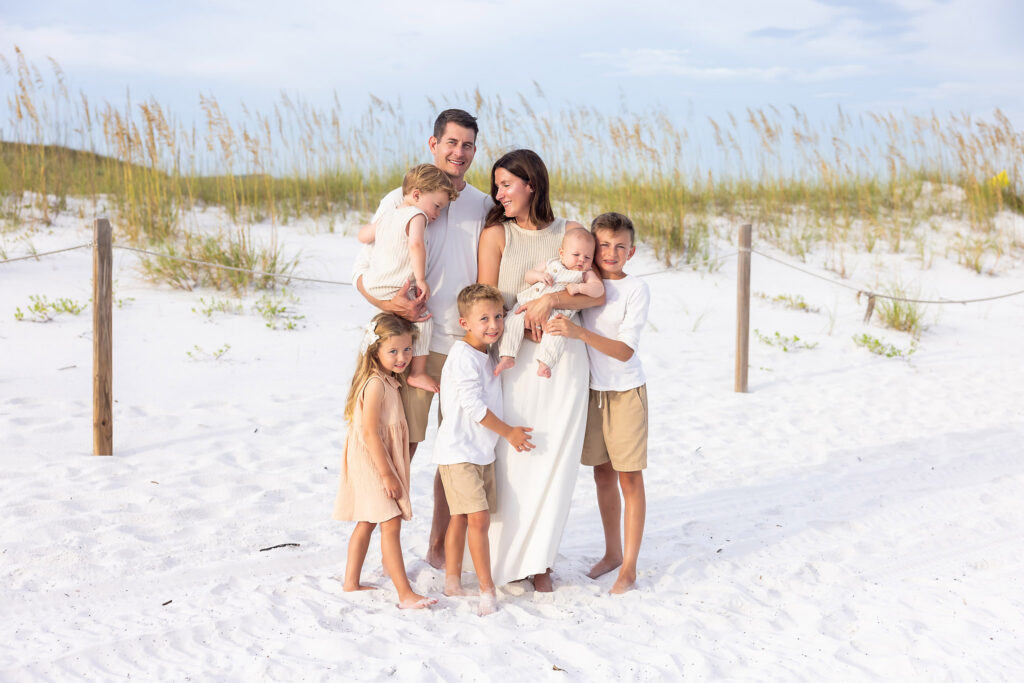 A family of 7 in a candid photograph wearing khaki and creams on the beach at Grayton State Park in front of the dunes.