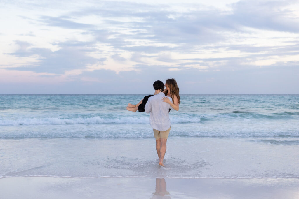 man carrying new fiance into the gulf after proposing on the beaches of 30a.