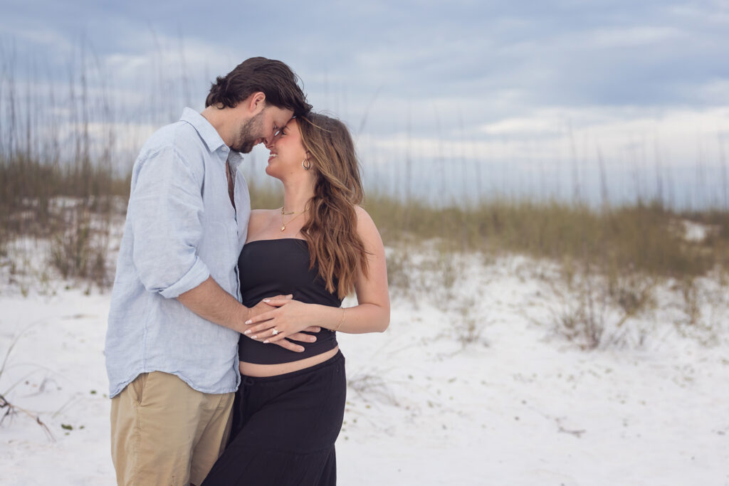 Newly engaged couple are expecting and posing for a photo in front of the sand dunes of Grayton Beach State Park.