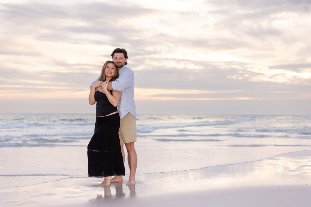 newly engaged couple posing for a photo in front of the Gulf of America on hwy 30a.