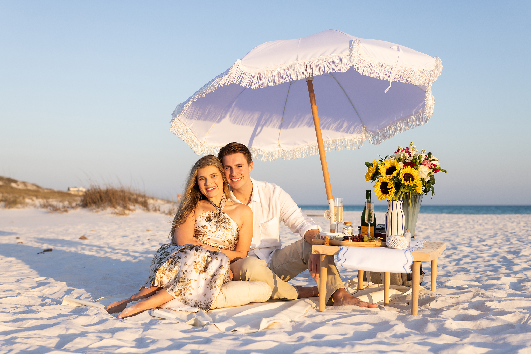 Surprise proposal set-up including boho umbrella, pillows, table, candles, champagne and flowers on 30a beach.
