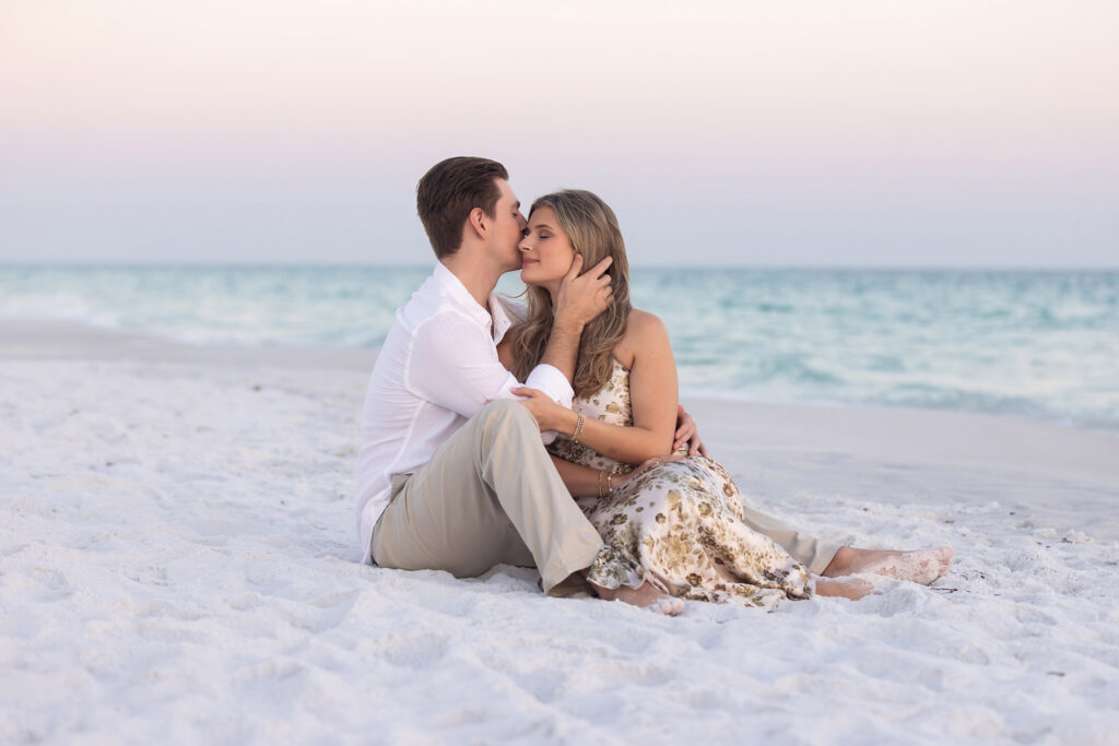 a sweet moment of a newly engaged couple sitting on sand on beach off of Hwy 30a at sunset.