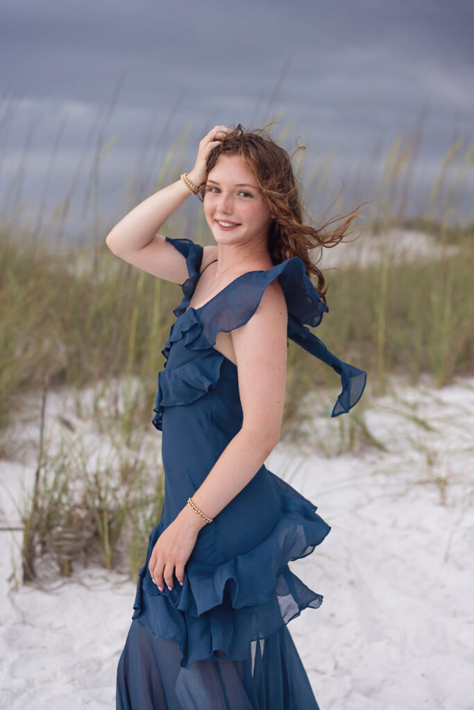 Young woman posing in blue long dress on beach for her senior portraits in Watercolor, Florida on 30a.